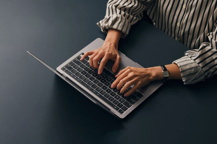 Top view of hands typing on a laptop keyboard, with only the hands and arms visible.