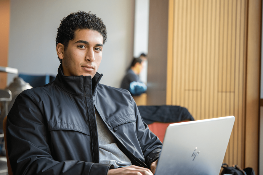 A student poses for a photograph while working at a laptop.