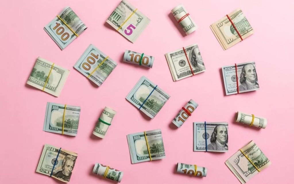 An assortment of $5, $10, $20, $50, and $100 bills against a pink background.