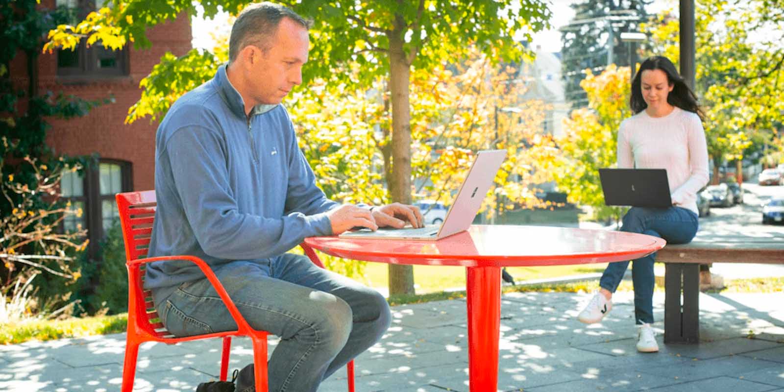 Students work on their laptops in an outdoor seating area.