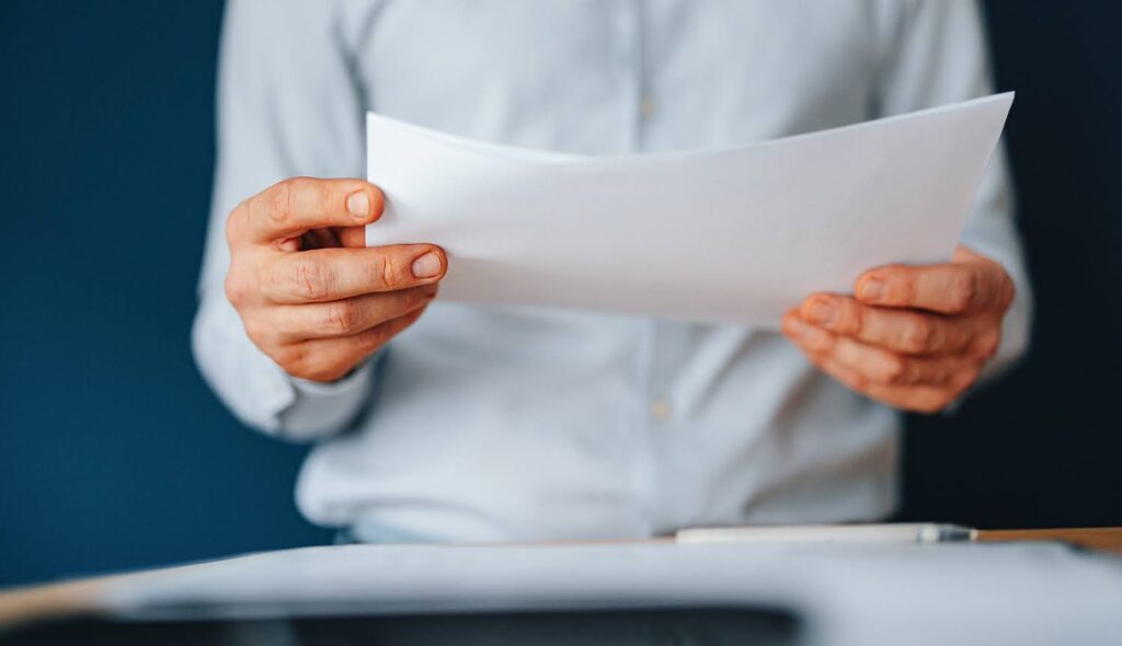 A person in a white shirt holds several sheets of paper, with only the back of the papers visible.