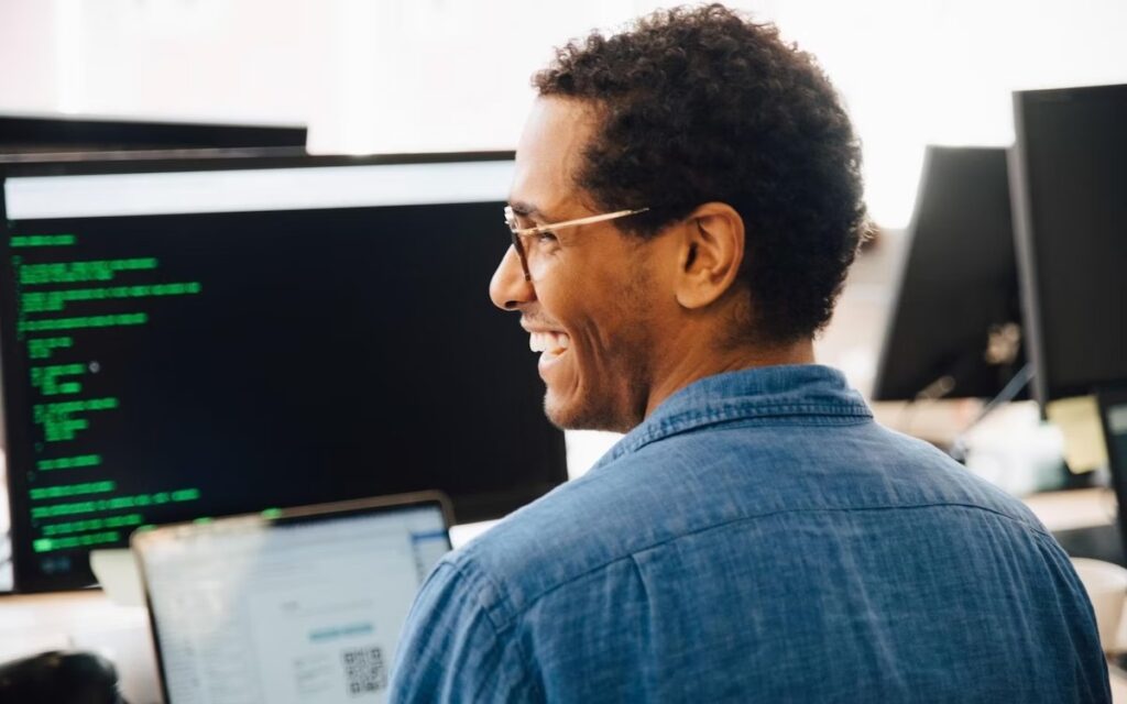 A person smiles while sitting in front of a computer.