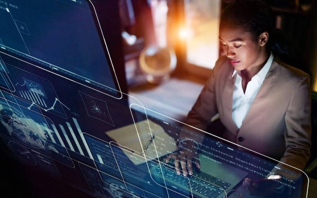 Images of computer screens with data appear in front of a woman wearing a brown blazer as she types on a computer keyboard.