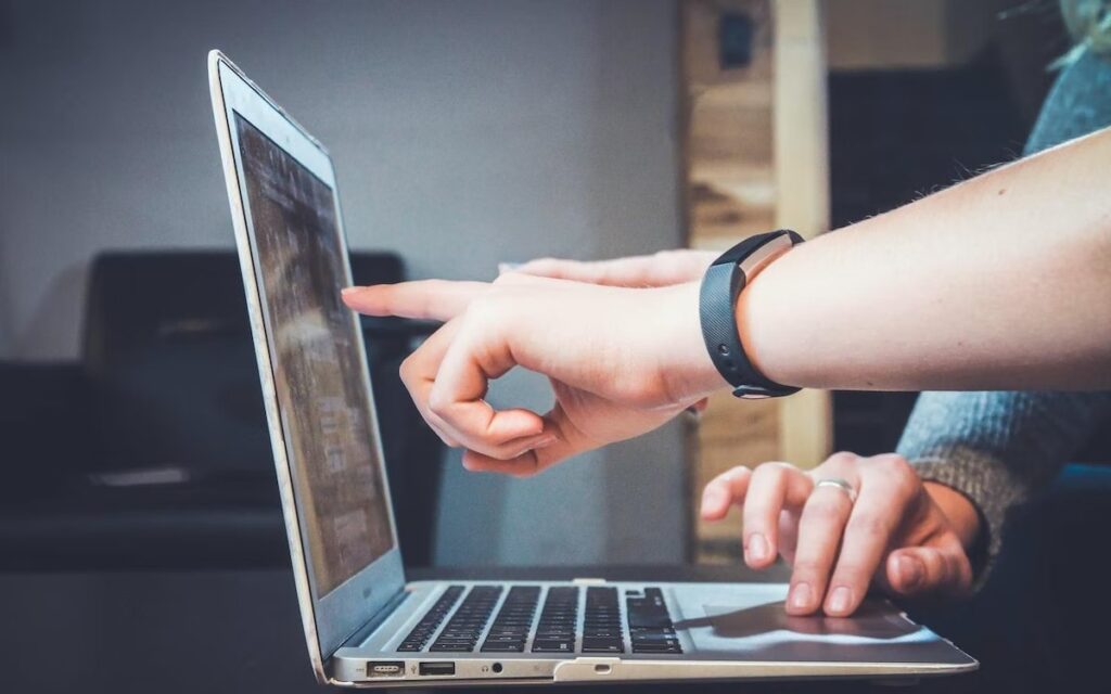 Two people point to an open computer screen.