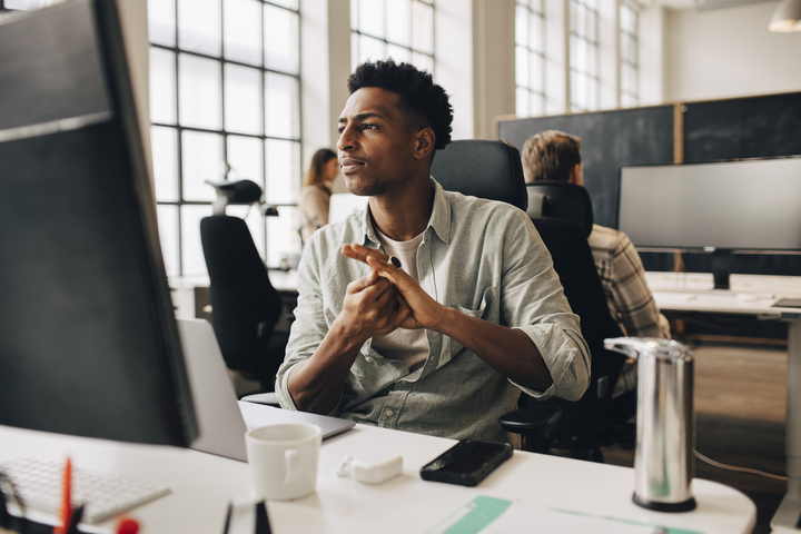 A young, Black data scientist in a tech office looks at something on his computer monitor.