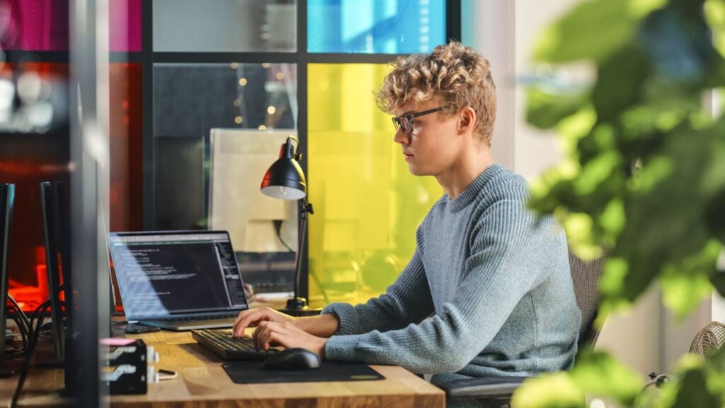 Side view of male data scientist in a stylish office writing lines of code on a desktop computer.