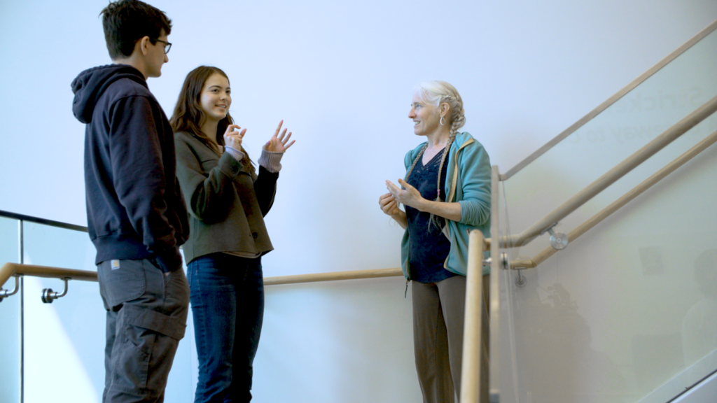 A diverse group of smiling students converse in an open-air stairwell.